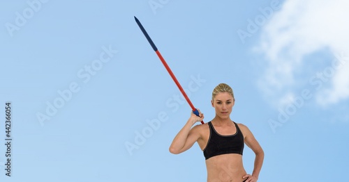 Portrait of caucasian female athlete holding a javelin against clouds in blue sky