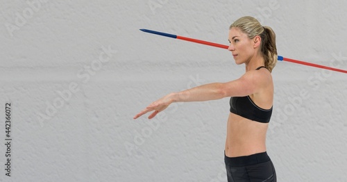 Concept side view of caucasian female athlete holding a javelin against grey background