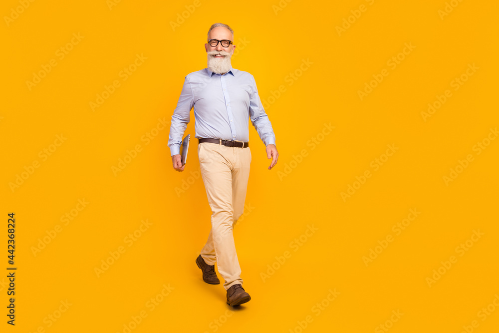 Full length photo of charming old man go good mood hold laptop smile cheerful isolated on yellow color background Full length photo of charming old man go good mood hold laptop smile cheerful isolated on yellow color background