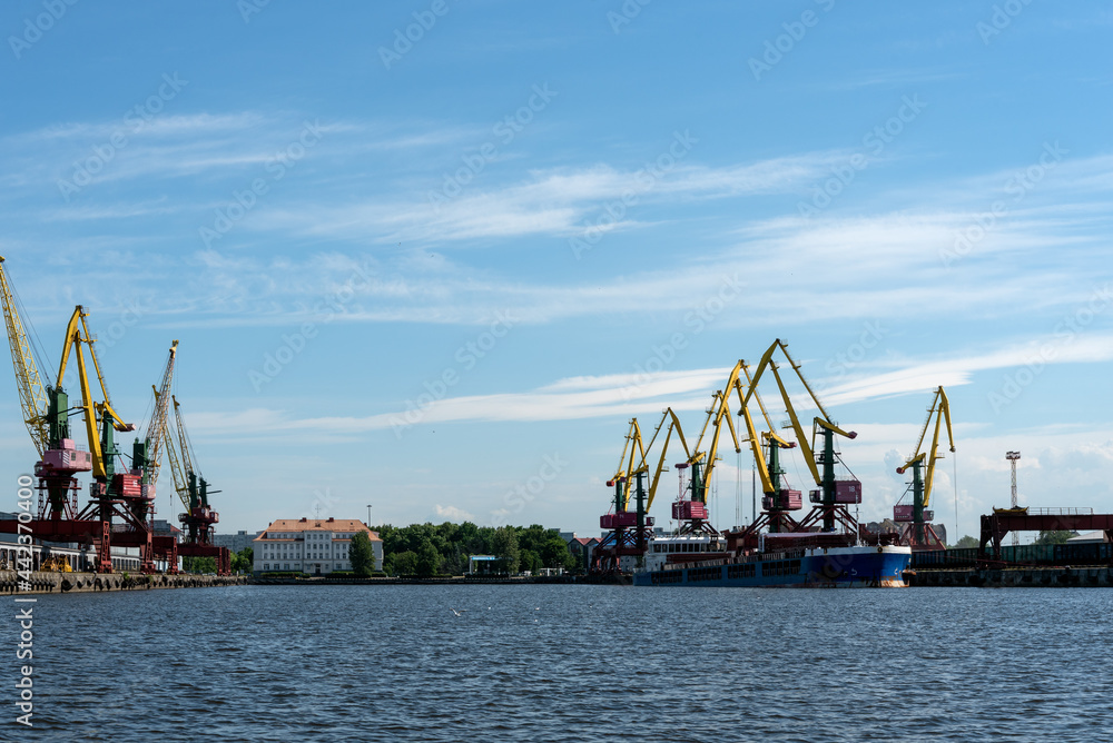 Many tall cargo cranes stand on the banks of the Venta River. Ventspils, Latvia, Baltic Sea.