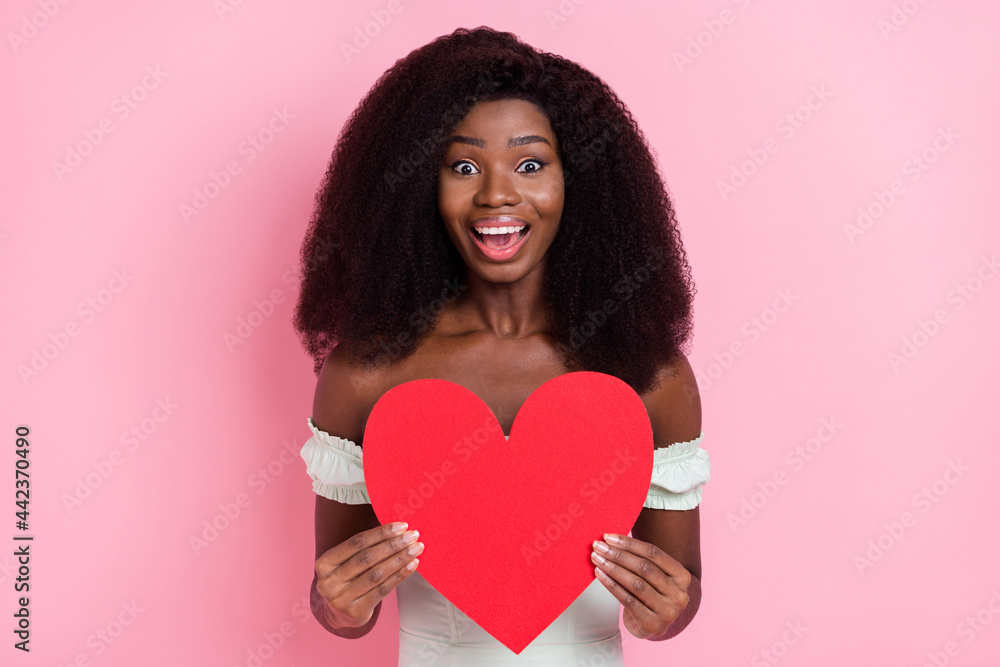Portrait of attractive amazed cheerful wavy-haired girl holding in hand heart shape amour isolated over pink pastel color background Portrait of attractive amazed cheerful wavy-haired girl holding in hand heart shape amour isolated over pink pastel color background