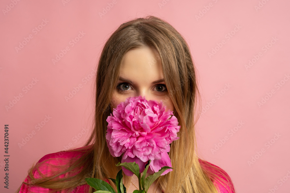 Close up photo of pretty blond woman posing with pion flower in stylish summer outfit over pink background. Close up photo of pretty blond woman posing with pion flower in stylish summer outfit over pink background.