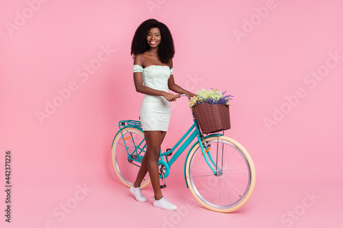 Fototapeta Naklejka Na Ścianę i Meble -  Full body profile side photo of young afro girl happy positive smile ride bicycle flower isolated over pink color background