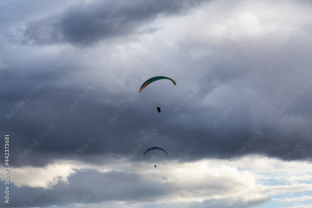 Adventurous People Flying on a Paraglider around the mountains. Savona, British Columbia, Canada. Adventurous People Flying on a Paraglider around the mountains. Savona, British Columbia, Canada.