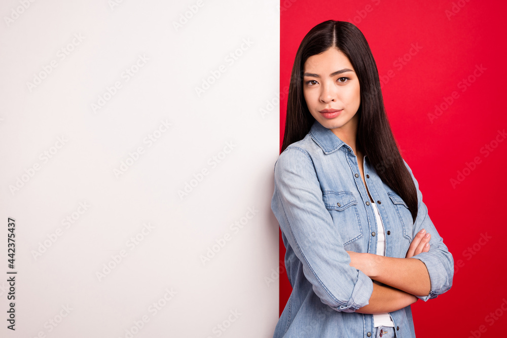 Portrait of attractive girl near big large blank poster ad information folded arms isolated over bright red color background Portrait of attractive girl near big large blank poster ad information folded arms isolated over bright red color background