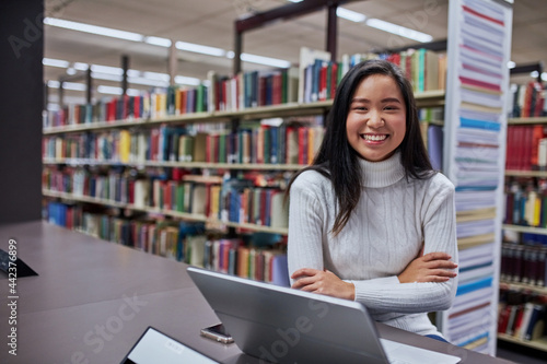 Young female Asian student working on her laptop at university library photo