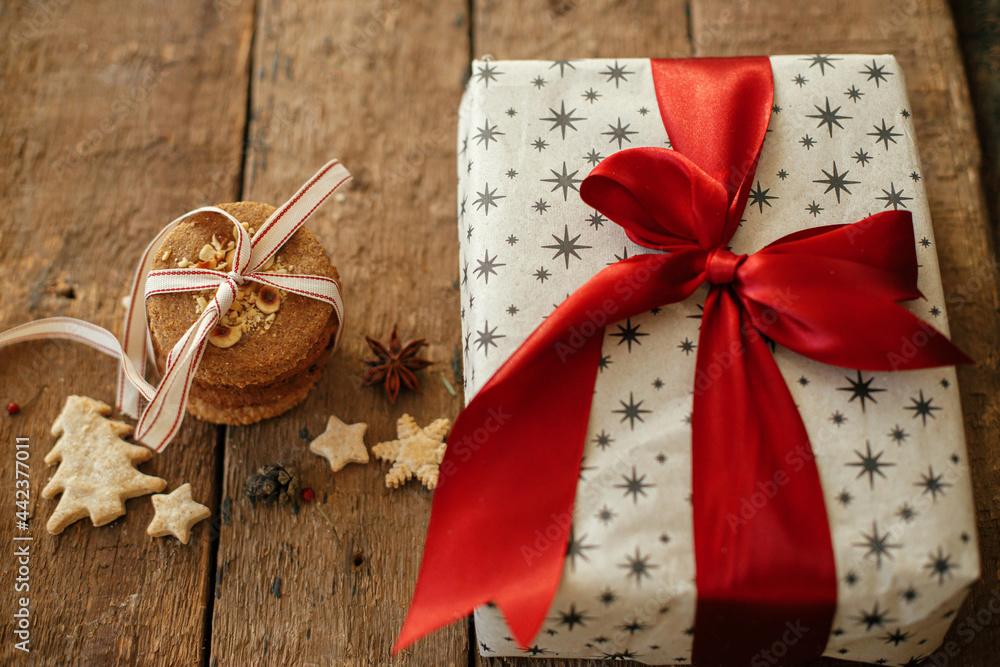 Christmas oatmeal cookies and stylish wrapped gift box with red ribbon on rustic wooden table. Xmas healthy cookies and present. Happy Holidays and Merry Christmas Christmas oatmeal cookies and stylish wrapped gift box with red ribbon on rustic wooden table. Xmas healthy cookies and present. Happy Holidays and Merry Christmas