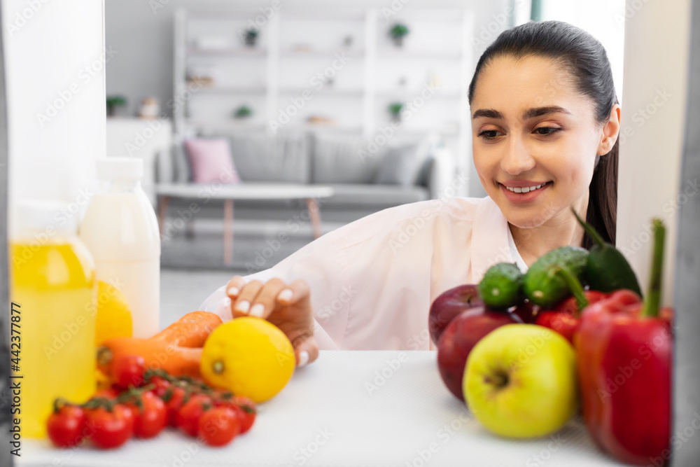Smiling woman opening fridge and taking food Smiling woman opening fridge and taking food