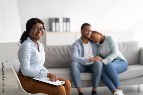 Fototapeta Naklejka Na Ścianę i Meble -  Cheerful female psychologist and young black couple hugging after effective therapy at office, copy space
