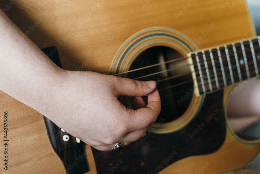 Fototapeta premium Young woman playing acoustic guitar at home. Happy girl enjoying music. Concept learning to play guitar. Female musician. Close-up of hands.