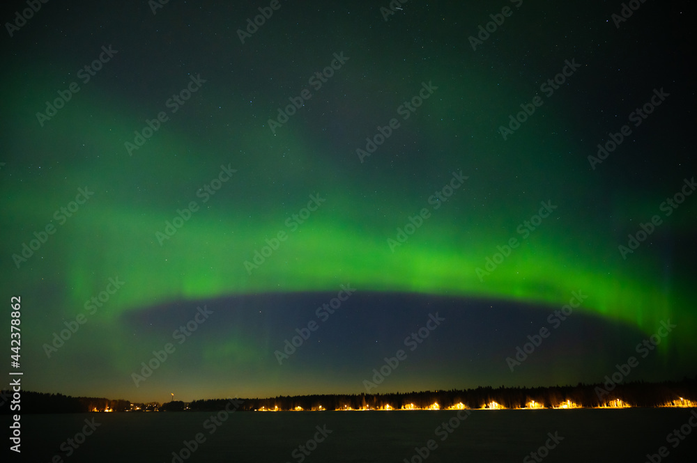 A green colour Aurora borealis on the starry night sky over a city. Aurora Borealis over Swedish lake Islands. Northern Sweden
