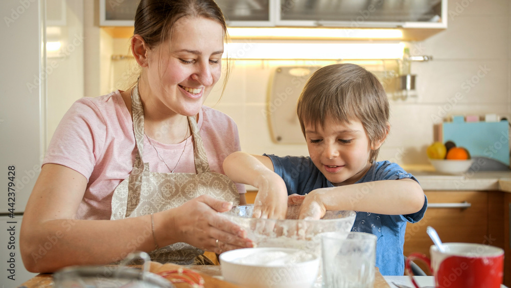Little boy helping his mother making dough and mixing it with hands. Children cooking with parents, little chef, family having time together, domestic kitchen.