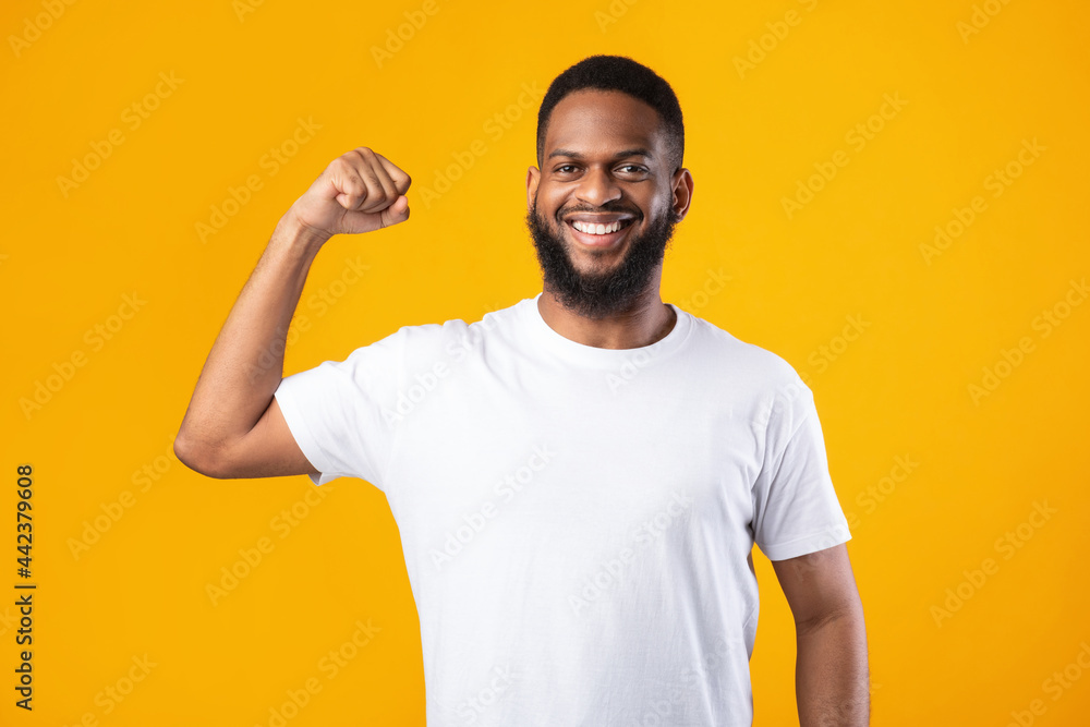 Cheerful Black Guy Showing Biceps Muscles Posing On Yellow Background Cheerful Black Guy Showing Biceps Muscles Posing On Yellow Background