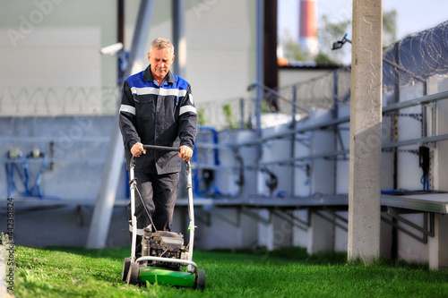 Obraz na plátně A pensioner in working clothes works with a lawn mower on the territory of the production base on a sunny day