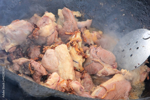 Large pieces of lamb meat with lamb fat dumba close-up fried in oil with bubbles in a black cauldron, cooking food