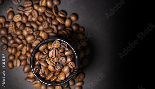 Ceramic cup with coffee beans on a blurred background from coffee beans scattered on a dark, top view, copy space. © Yarr