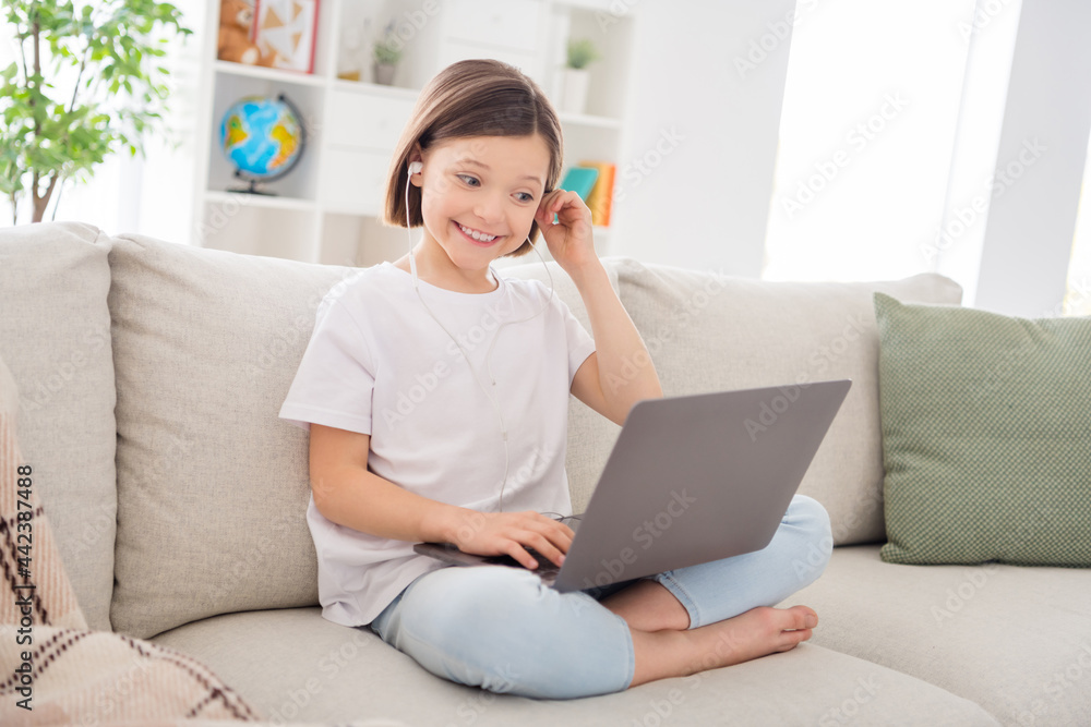 Photo of adorable shiny small schoolgirl dressed white t-shirt sitting coach listening modern gadget indoors room home house Photo of adorable shiny small schoolgirl dressed white t-shirt sitting coach listening modern gadget indoors room home house