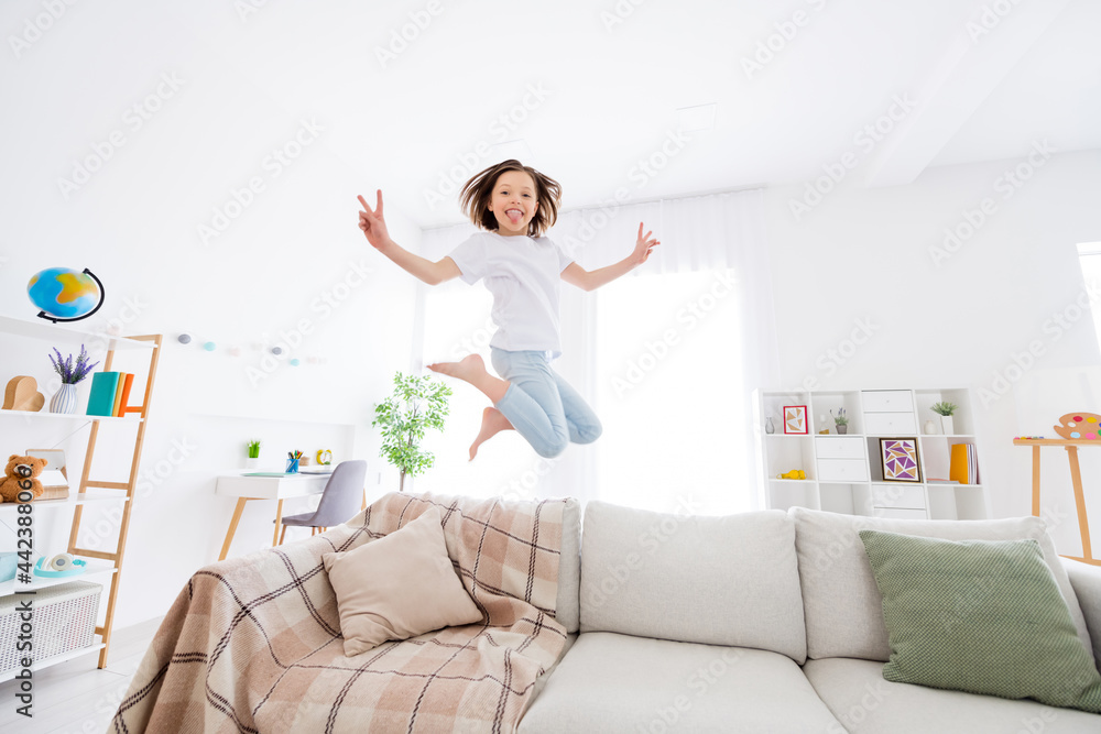 Full size profile side photo of young little girl happy positive smile jump show peace cool v-sign tongue-out grimace home Full size profile side photo of young little girl happy positive smile jump show peace cool v-sign tongue-out grimace home