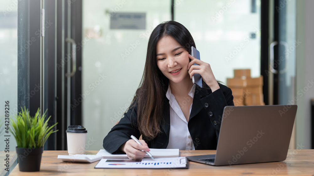Charming Asian businesswoman talking on the phone and pointing graph at statistical concept work analysis at the office. Charming Asian businesswoman talking on the phone and pointing graph at statistical concept work analysis at the office.