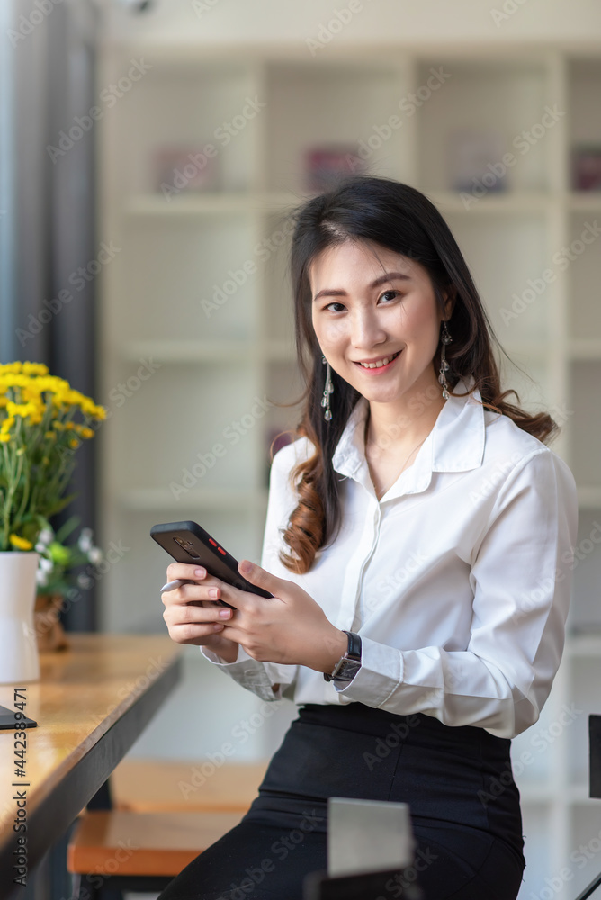 Asian businesswoman looking at the camera in hand holding smartphone at the office. Asian businesswoman looking at the camera in hand holding smartphone at the office.