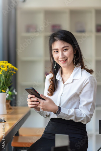 Asian businesswoman looking at the camera in hand holding smartphone at the office.