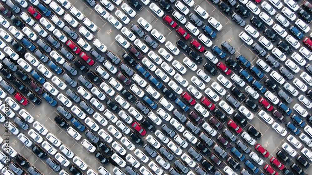 New multi-colored passenger cars are standing in straight diagonal rows in a giant parking lot on the territory of the plant, aerial view New multi-colored passenger cars are standing in straight diagonal rows in a giant parking lot on the territory of the plant, aerial view