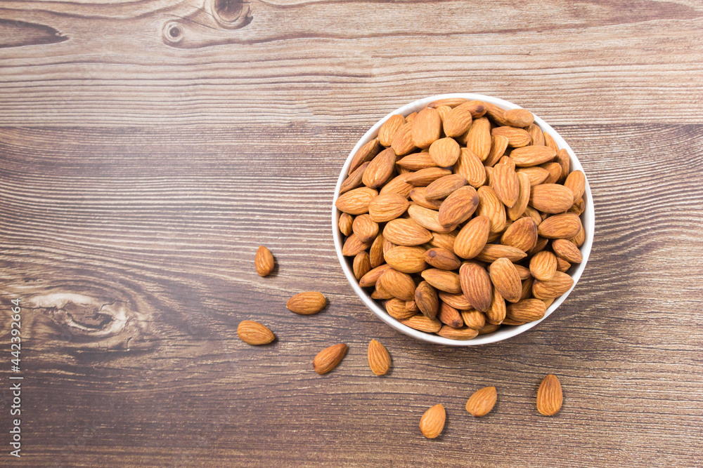 Almond nuts in a white bowl on wooden background, top view, flat lay, top-down, selective focus.copy space. Almond nuts in a white bowl on wooden background, top view, flat lay, top-down, selective focus.copy space.