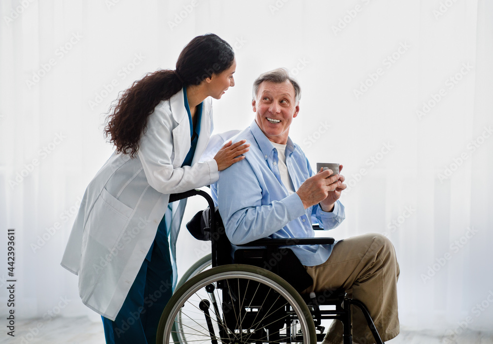 Young female doctor helping senior handicapped man in wheelchair, taking care of older patient at retirement home Young female doctor helping senior handicapped man in wheelchair, taking care of older patient at retirement home