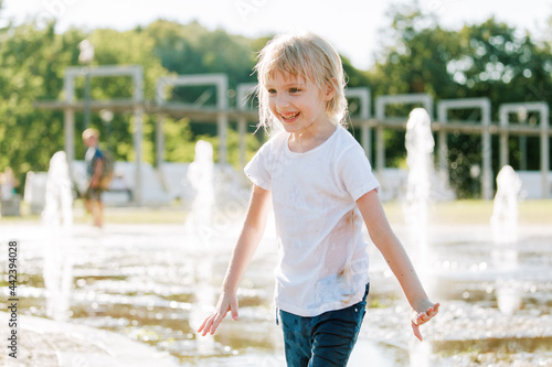 Obraz na płótnie Cute cheerful girl playing in fountain. Kid in white shirt having fun in summer park w salonie