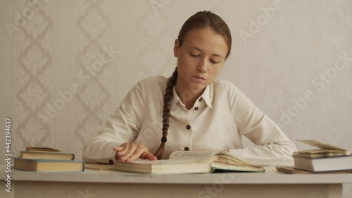 Young woman quickly flips through the book looking for right page. Student sitting at the table at home, preparing for exam, doing homework, looking for information in scientific literature. Education