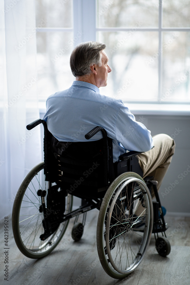 Full length of impaired senior man in wheelchair feeling depressed, suffering from loneliness in retirement home