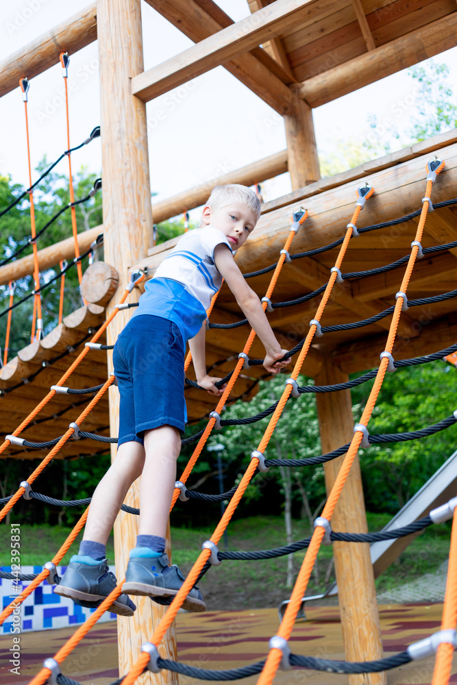 a child boy climbs a cable ladder on a wooden ecological playground in summer a child boy climbs a cable ladder on a wooden ecological playground in summer