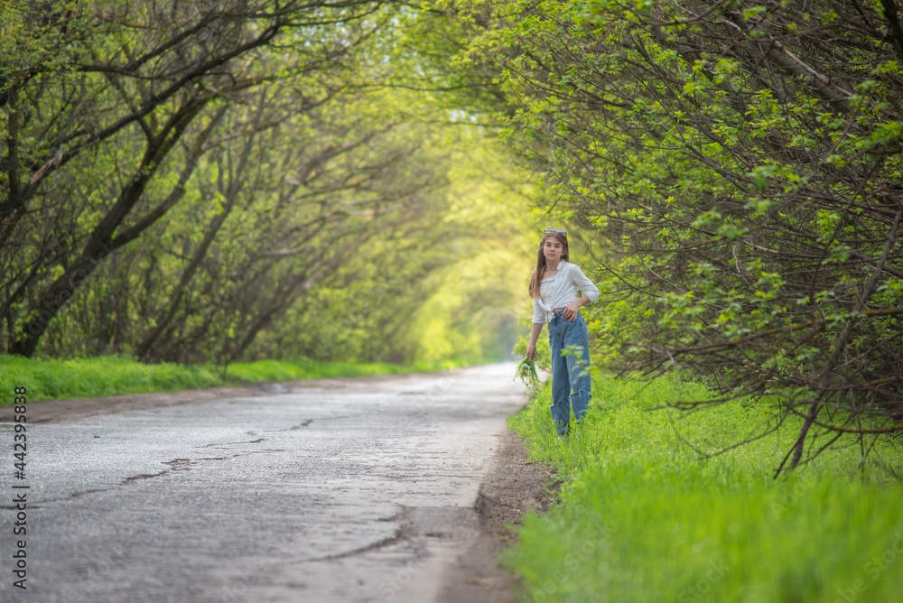 Obraz premium fashionable little girl standing walking on the road against the background of an arch of green branchy trees
