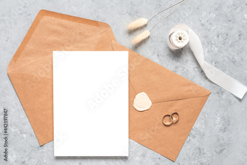 Autumn wedding template with stationery set. Blank greeting card mock up, brown envelopes, wedding rings and dry grass. Top view, flat lay.