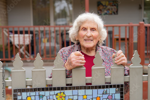 An elderly lady smiling over the top of her front fence photo