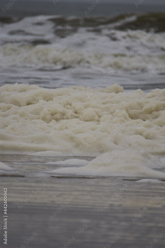 Waves and sea foam on a beach of the North Sea on a cloudy day Waves and sea foam on a beach of the North Sea on a cloudy day