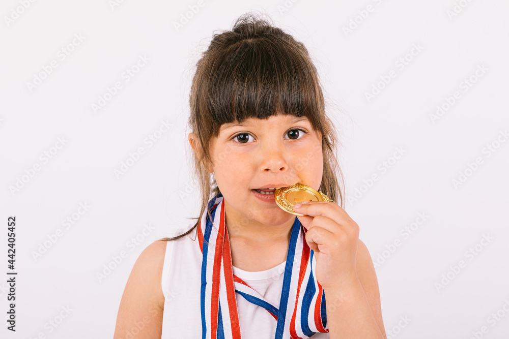 Little brown-haired girl with sports champion medals, biting them. Sport and victory concept Little brown-haired girl with sports champion medals, biting them. Sport and victory concept