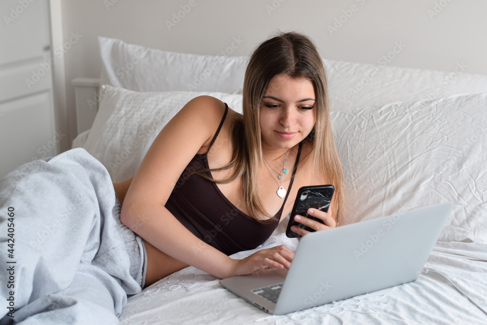 Young teenage girl laying on a bed using laptop computer and mobile phone Young teenage girl laying on a bed using laptop computer and mobile phone