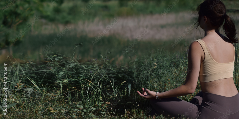 Young woman sitting in a yoga meditation lotus position outdoors in nature web banner