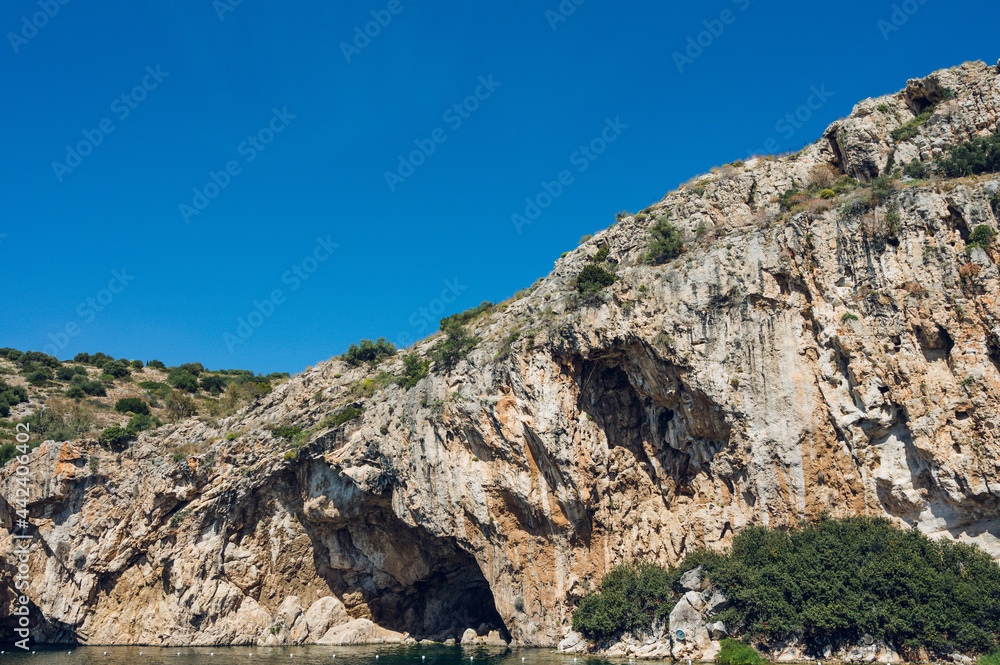 Vouliagmeni lake in Greece at sunny summer day. Small brackish-water lake fed. Scenic landscape of white mountain and green water. Thermal spring. SPA.