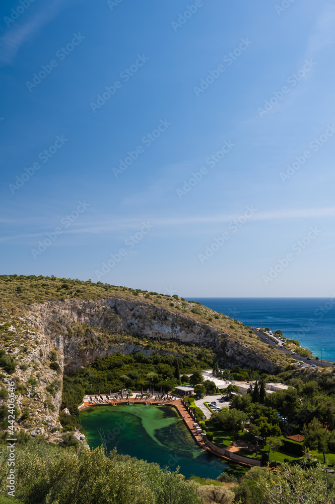 Vouliagmeni lake in Greece at sunny summer day. Small brackish-water lake fed. Scenic landscape of white mountain and green water. Thermal spring. View from above.
