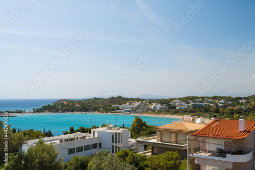 Cityscape of sea shore in Greece. Top view. Urban architecture and a lot of green trees. Hilly area. Sunne day. Aegean sea.
