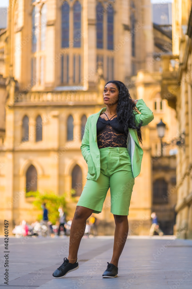 Fototapeta premium Lifestyle of a young girl of black African ethnicity with a beautiful green suit. Sightseeing in the city walking next to a cathedral