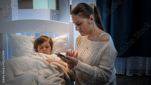 Canvas Print Young mother worrying about her sick son sleeping in bed calling doctor