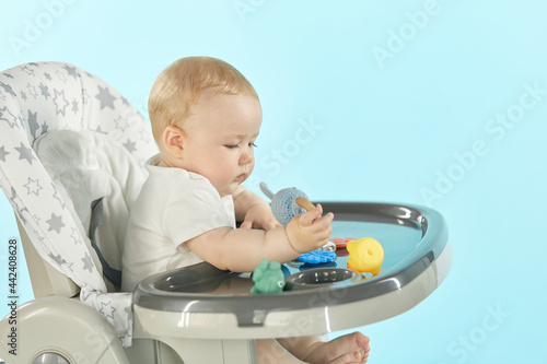 Close-up of the side of the baby sitting on a high chair playing with toys. The baby is waiting in a feeding chair on an isolated background. Suitable for advertising baby food. Place to copy text