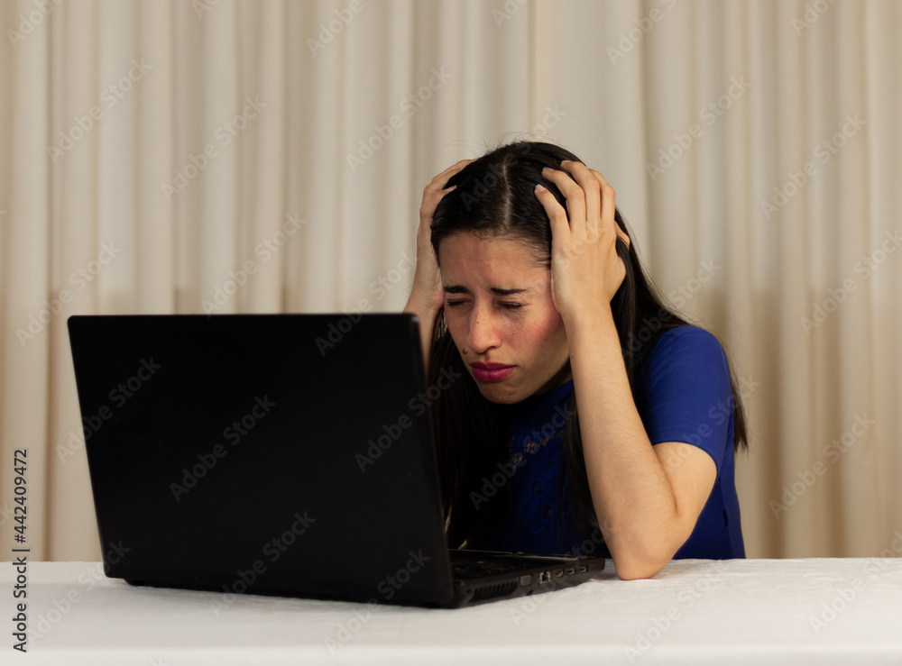 Woman sitting in front of her laptop. looking at the screen, WORRIED, scared, hands on head, crying, sad. Latin woman in front of her laptop. Woman sitting in front of her laptop. looking at the screen, WORRIED, scared, hands on head, crying, sad. Latin woman in front of her laptop.