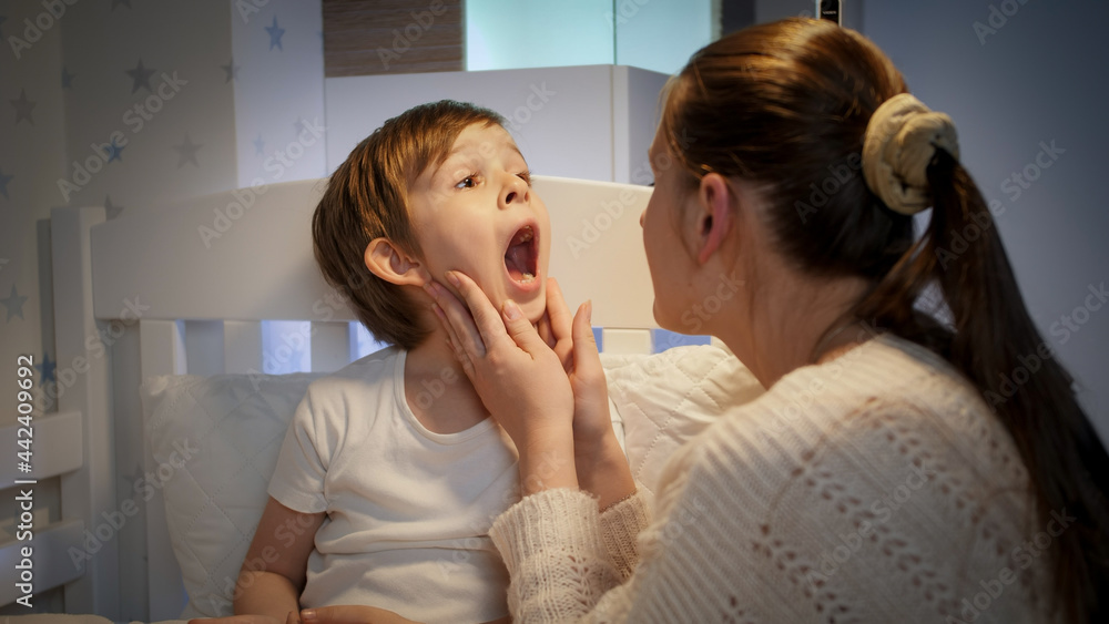 Caring mother checking and examining soring throat of her sick little son in bed. Concept of children illness, disease and parent care Caring mother checking and examining soring throat of her sick little son in bed. Concept of children illness, disease and parent care