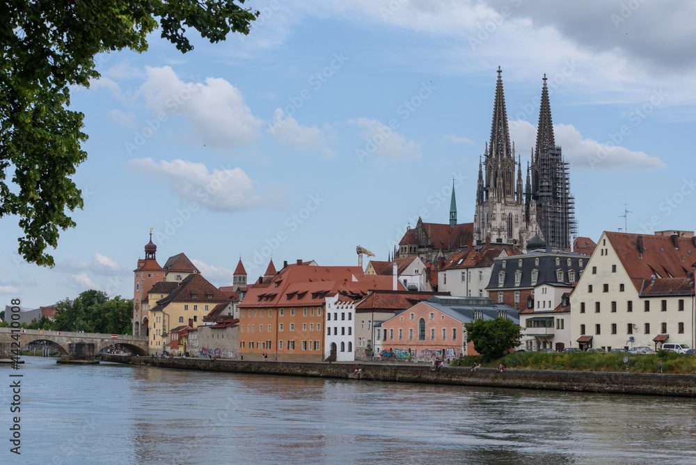Fototapeta premium Blick von der Wöhrd auf Dom, steinerne Brücke , Rathausturm und Ufer mit Wolken am Himmel und Bäumen im Vordergrund
