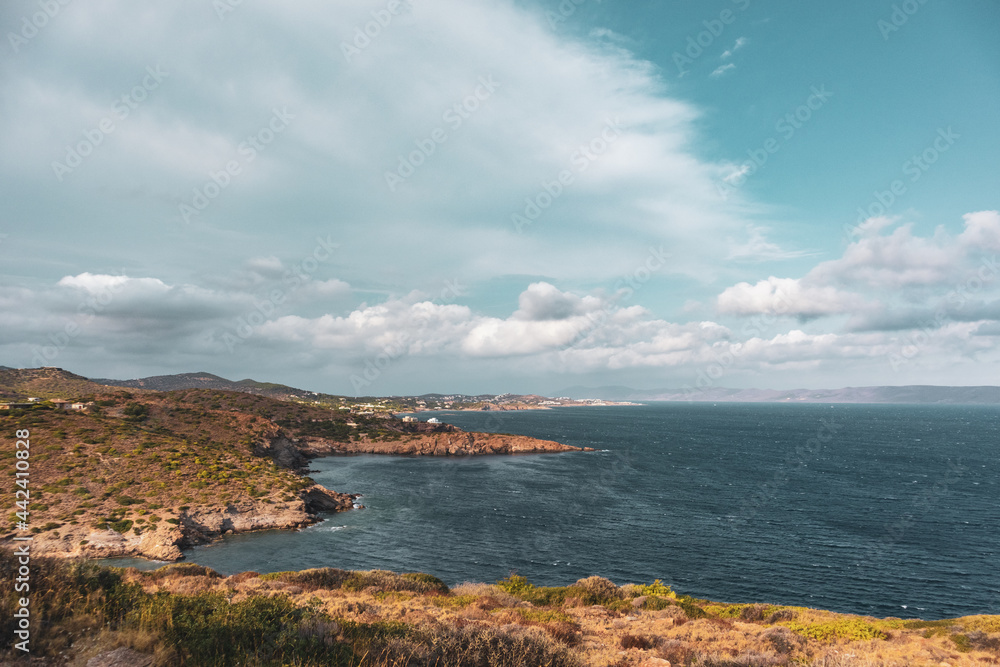 Rocky cliffs, sea shore line landscape near Athens. View from Cape Sounion. Vibrant colorful view with scenic clouds and blue Mediterranean stormy sea. Color graded