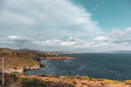 Rocky cliffs, sea shore line landscape near Athens. View from Cape Sounion. Vibrant colorful view with scenic clouds and blue Mediterranean stormy sea. Color graded © Kathrine Andi